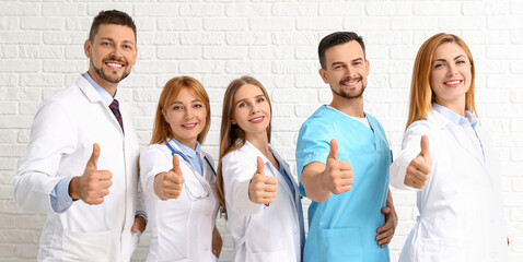 Team of doctors showing thumb-up gesture on white brick background