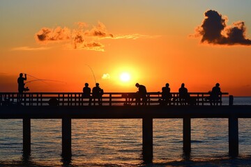 Obraz premium Evening sunset on the pier with people fishing and enjoying the tranquil coastal atmosphere, Tranquil lifestyle evening sunset scene of people relax and fishing on pier