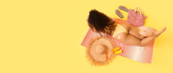 Young woman with beach accessories lying on yellow background with space for text, top view