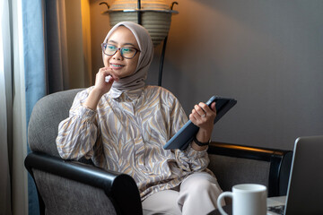 Asian Indonesian Muslim Woman Working from Home Using a Digital Tablet