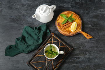 Teapot with cup of fresh mint tea, lemon and cinnamon on grunge black background