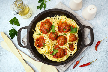 Frying pan of boiled pasta with tomato sauce and meat balls on white table