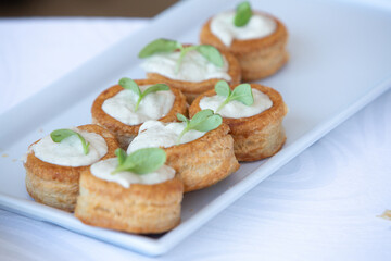 Delicious vol-au-vents with cream cheese topping and herbs garnishing a white rectangular plate