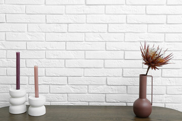 Vase with dried red protea and candles on dresser near white brick wall