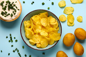 Bowl of tasty sour cream with sliced green onion and potato chips on blue background