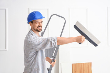 Male decorator with putty knife and stepladder in room