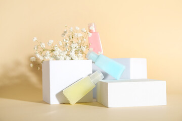 Composition with bottles of cosmetic products, plaster podiums and gypsophila flowers on color...