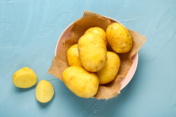 Bowl with raw baby potatoes on blue background