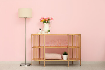 Chest of drawers with floor lamp, houseplants and stylish decor in shape of word HOME near pink wall