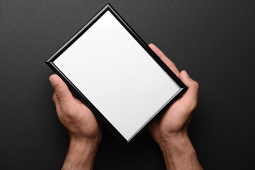 Man holding blank photo frame on black background