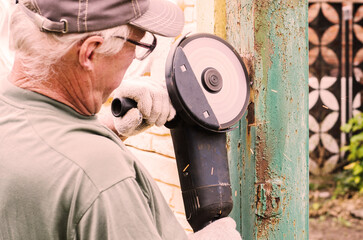 Senior man using angle grinder to clean rusty green metal pole outdoors