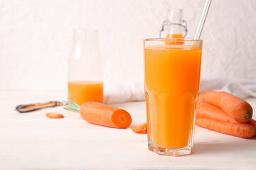 Glass and bottle of fresh carrot juice on white wooden table