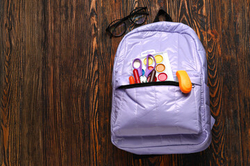 Lilac school backpack with eyeglasses, watercolors and scissors on wooden background