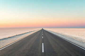 Endless asphalt road through pink salt flats at sunset