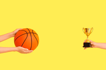 Female hands with gold cup and basketball on yellow background