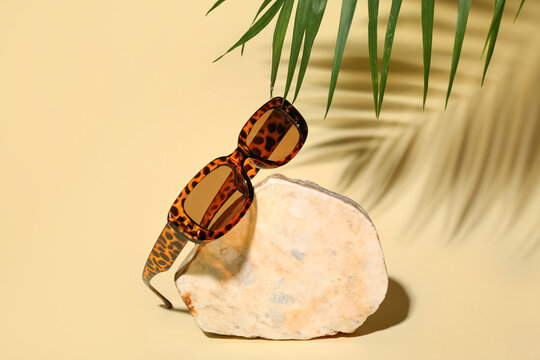 Stone with stylish sunglasses and palm leaf on yellow background - Powered by Adobe