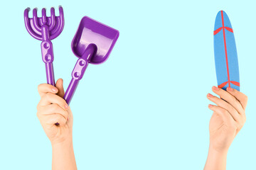 Female hands with mini surfboard and beach sand toys on blue background