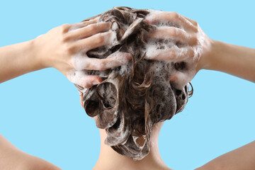 Young woman washing hair on blue background, back view