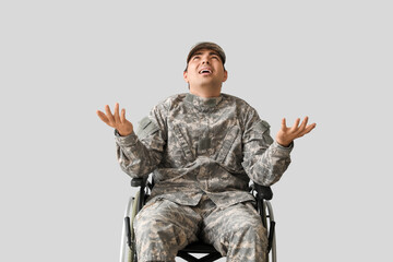 Upset young soldier in wheelchair on light background