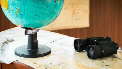 Binoculars on a conservationist's desk with a blurred globe next to it, the concept of wildlife conservation or conservation of an area from encroachment.