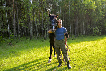 rustic man with  horse in rural village near  forest.  horse farm is surrounded by nature, hay is stacked nearby,  peaceful and traditional.  man is caring for  horse
