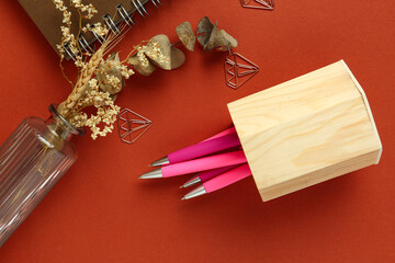Vase of dried flowers, wooden holder with pens and notebook on red background