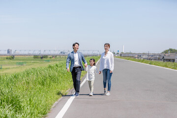 手を繋いで土手を歩く家族