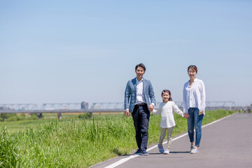 Fototapeta premium 手を繋いで土手を歩く家族