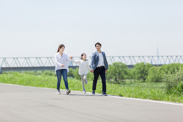手を繋いで土手を歩く家族