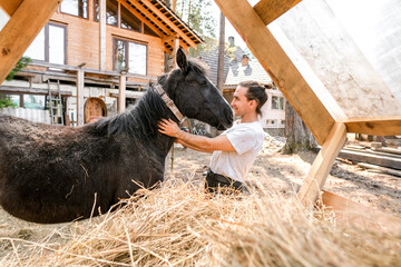 rustic man with  horse in rural village near  forest.  horse farm is surrounded by nature, hay is stacked nearby,  peaceful and traditional.  man is caring for  horse