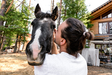rustic man with  horse in rural village near  forest.  horse farm is surrounded by nature, hay is stacked nearby,  peaceful and traditional.  man is caring for  horse