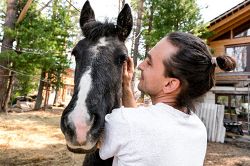 rustic man with  horse in rural village near  forest.  horse farm is surrounded by nature, hay is stacked nearby,  peaceful and traditional.  man is caring for  horse