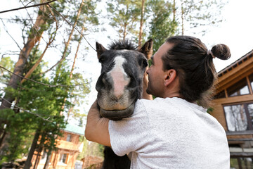 rustic man with  horse in rural village near  forest.  horse farm is surrounded by nature, hay is stacked nearby,  peaceful and traditional.  man is caring for  horse