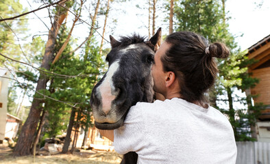 rustic man with  horse in rural village near  forest.  horse farm is surrounded by nature, hay is stacked nearby,  peaceful and traditional.  man is caring for  horse