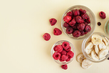 Bowls with tasty freeze-dried banana, cherries and raspberries on beige background