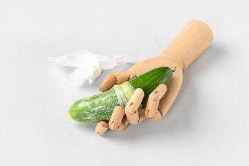 Wooden hand with fresh cucumber in condom and used tissue on white background. Sex education