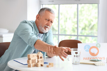 Senior man suffering from Parkinson syndrome at table in kitchen
