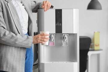 Businesswoman pouring water from cooler in office, closeup