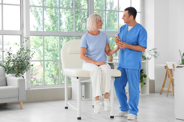 Male endocrinologist with lancet pen measuring blood sugar level of mature woman in clinic