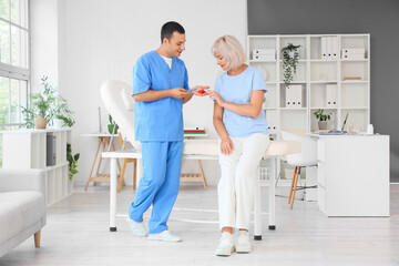 Obraz premium Male endocrinologist showing thyroid gland model to mature woman in clinic