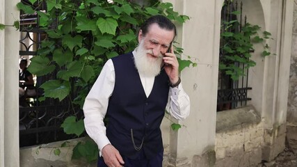 Old man in traditional cultural attire enjoying friendly phone conversation amidst lush greenery - Powered by Adobe