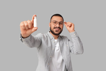 Young man in eyeglasses holding eye drops on grey background