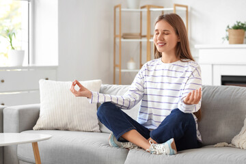 Obraz premium Young woman meditating on sofa at home