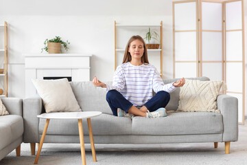 Young woman meditating on sofa at home