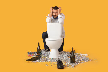 Young man feeling unwell near toilet bowl after Christmas party on yellow background