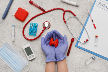 Doctor holding thyroid gland model and medical supplies on grunge background. Endocrinology concept