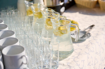 refreshing lemonade pitchers and empty glasses on sunny outdoor event table evoke summer vibes,...