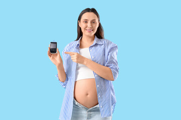 Young pregnant woman pointing at glucometer on blue background. Gestational diabetes concept