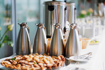 coffee break essentials with stainless steel thermoses and assorted pastries in bright conference setting. ideal corporate meeting catering concept emphasizing convenience and hospitality