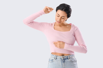 Young African-American woman checking her breast on white background. Cancer awareness concept